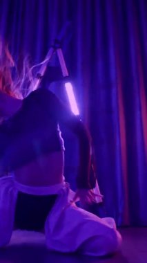 Dikey. Baştan çıkarıcı dans eden seksi kadın. Titreyen bir dansçı, canlı mor ve mavi ışıkla yıkanmış, canlı neon bir üçgenin altında sahnenin enerjisini somutlaştırıyor. Bir sanatçının kadın vücudu.