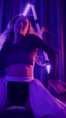 Dikey. Baştan çıkarıcı dans eden seksi kadın. Titreyen bir dansçı, canlı mor ve mavi ışıkla yıkanmış, canlı neon bir üçgenin altında sahnenin enerjisini somutlaştırıyor. Bir sanatçının kadın vücudu.