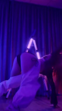 Dikey. Baştan çıkarıcı dans eden seksi kadın. Titreyen bir dansçı, canlı mor ve mavi ışıkla yıkanmış, canlı neon bir üçgenin altında sahnenin enerjisini somutlaştırıyor. Bir sanatçının kadın vücudu.