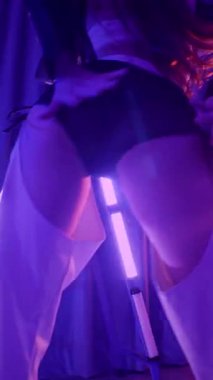 Dikey. Baştan çıkarıcı dans eden seksi kadın. Titreyen bir dansçı, canlı mor ve mavi ışıkla yıkanmış, canlı neon bir üçgenin altında sahnenin enerjisini somutlaştırıyor. Bir sanatçının kadın vücudu.