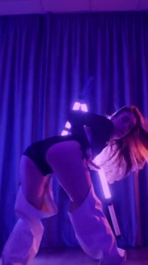 Dikey. Baştan çıkarıcı dans eden seksi kadın. Titreyen bir dansçı, canlı mor ve mavi ışıkla yıkanmış, canlı neon bir üçgenin altında sahnenin enerjisini somutlaştırıyor. Bir sanatçının kadın vücudu.