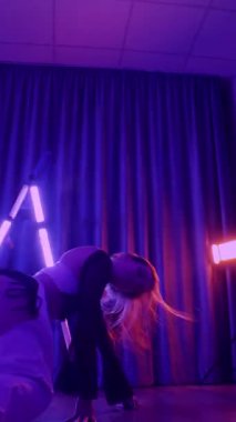 Dikey. Baştan çıkarıcı dans eden seksi kadın. Titreyen bir dansçı, canlı mor ve mavi ışıkla yıkanmış, canlı neon bir üçgenin altında sahnenin enerjisini somutlaştırıyor. Bir sanatçının kadın vücudu.