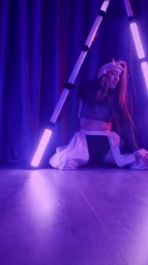 Dikey. Baştan çıkarıcı dans eden seksi kadın. Titreyen bir dansçı, canlı mor ve mavi ışıkla yıkanmış, canlı neon bir üçgenin altında sahnenin enerjisini somutlaştırıyor. Bir sanatçının kadın vücudu.