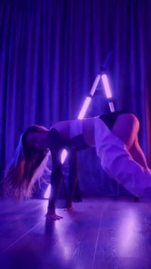 Dikey. Baştan çıkarıcı dans eden seksi kadın. Titreyen bir dansçı, canlı mor ve mavi ışıkla yıkanmış, canlı neon bir üçgenin altında sahnenin enerjisini somutlaştırıyor. Bir sanatçının kadın vücudu.