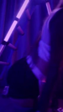 Dikey. Baştan çıkarıcı dans eden seksi kadın. Titreyen bir dansçı, canlı mor ve mavi ışıkla yıkanmış, canlı neon bir üçgenin altında sahnenin enerjisini somutlaştırıyor. Bir sanatçının kadın vücudu.