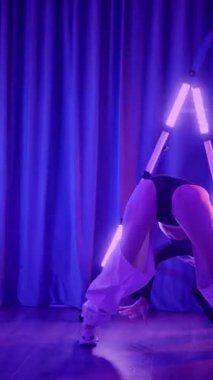 Dikey. Baştan çıkarıcı dans eden seksi kadın. Titreyen bir dansçı, canlı mor ve mavi ışıkla yıkanmış, canlı neon bir üçgenin altında sahnenin enerjisini somutlaştırıyor. Bir sanatçının kadın vücudu.