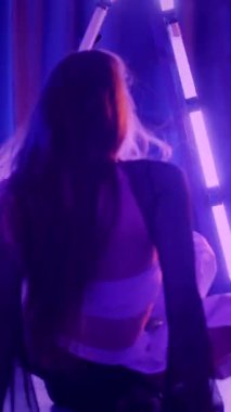 Dikey. Baştan çıkarıcı dans eden seksi kadın. Titreyen bir dansçı, canlı mor ve mavi ışıkla yıkanmış, canlı neon bir üçgenin altında sahnenin enerjisini somutlaştırıyor. Bir sanatçının kadın vücudu.