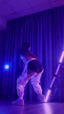 Dikey. Baştan çıkarıcı dans eden seksi kadın. Titreyen bir dansçı, canlı mor ve mavi ışıkla yıkanmış, canlı neon bir üçgenin altında sahnenin enerjisini somutlaştırıyor. Bir sanatçının kadın vücudu.