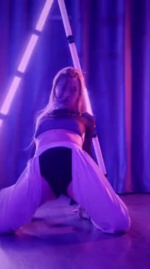 Dikey. Baştan çıkarıcı dans eden seksi kadın. Titreyen bir dansçı, canlı mor ve mavi ışıkla yıkanmış, canlı neon bir üçgenin altında sahnenin enerjisini somutlaştırıyor. Bir sanatçının kadın vücudu.