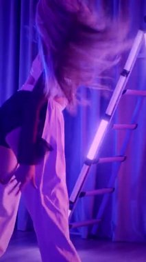 Dikey. Baştan çıkarıcı dans eden seksi kadın. Titreyen bir dansçı, canlı mor ve mavi ışıkla yıkanmış, canlı neon bir üçgenin altında sahnenin enerjisini somutlaştırıyor. Bir sanatçının kadın vücudu.