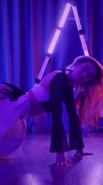 Dikey. Baştan çıkarıcı dans eden seksi kadın. Titreyen bir dansçı, canlı mor ve mavi ışıkla yıkanmış, canlı neon bir üçgenin altında sahnenin enerjisini somutlaştırıyor. Bir sanatçının kadın vücudu.