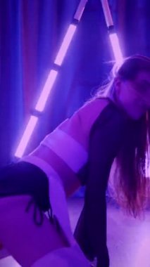 Dikey. Baştan çıkarıcı dans eden seksi kadın. Titreyen bir dansçı, canlı mor ve mavi ışıkla yıkanmış, canlı neon bir üçgenin altında sahnenin enerjisini somutlaştırıyor. Bir sanatçının kadın vücudu.