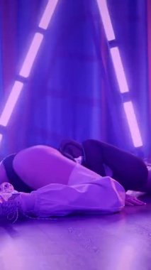 Dikey. Baştan çıkarıcı dans eden seksi kadın. Titreyen bir dansçı, canlı mor ve mavi ışıkla yıkanmış, canlı neon bir üçgenin altında sahnenin enerjisini somutlaştırıyor. Bir sanatçının kadın vücudu.