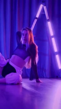 Dikey. Baştan çıkarıcı dans eden seksi kadın. Titreyen bir dansçı, canlı mor ve mavi ışıkla yıkanmış, canlı neon bir üçgenin altında sahnenin enerjisini somutlaştırıyor. Bir sanatçının kadın vücudu.