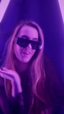 Dikey. Baştan çıkarıcı dans eden seksi kadın. Titreyen bir dansçı, canlı mor ve mavi ışıkla yıkanmış, canlı neon bir üçgenin altında sahnenin enerjisini somutlaştırıyor. Bir sanatçının kadın vücudu.