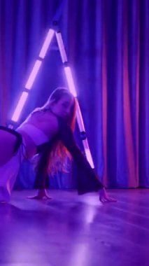 Dikey. Baştan çıkarıcı dans eden seksi kadın. Titreyen bir dansçı, canlı mor ve mavi ışıkla yıkanmış, canlı neon bir üçgenin altında sahnenin enerjisini somutlaştırıyor. Bir sanatçının kadın vücudu.