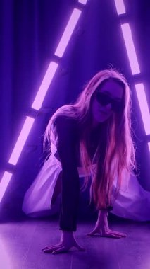 Dikey. Baştan çıkarıcı dans eden seksi kadın. Titreyen bir dansçı, canlı mor ve mavi ışıkla yıkanmış, canlı neon bir üçgenin altında sahnenin enerjisini somutlaştırıyor. Bir sanatçının kadın vücudu.