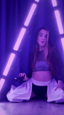 Dikey. Baştan çıkarıcı dans eden seksi kadın. Titreyen bir dansçı, canlı mor ve mavi ışıkla yıkanmış, canlı neon bir üçgenin altında sahnenin enerjisini somutlaştırıyor. Bir sanatçının kadın vücudu.