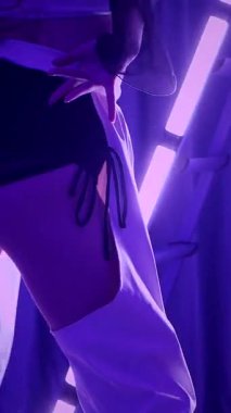 Dikey. Baştan çıkarıcı dans eden seksi kadın. Titreyen bir dansçı, canlı mor ve mavi ışıkla yıkanmış, canlı neon bir üçgenin altında sahnenin enerjisini somutlaştırıyor. Bir sanatçının kadın vücudu.