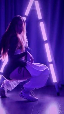 Dikey. Baştan çıkarıcı dans eden seksi kadın. Titreyen bir dansçı, canlı mor ve mavi ışıkla yıkanmış, canlı neon bir üçgenin altında sahnenin enerjisini somutlaştırıyor. Bir sanatçının kadın vücudu.