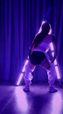 Dikey. Baştan çıkarıcı dans eden seksi kadın. Titreyen bir dansçı, canlı mor ve mavi ışıkla yıkanmış, canlı neon bir üçgenin altında sahnenin enerjisini somutlaştırıyor. Bir sanatçının kadın vücudu.