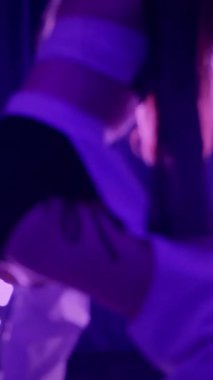 Dikey. Baştan çıkarıcı dans eden seksi kadın. Titreyen bir dansçı, canlı mor ve mavi ışıkla yıkanmış, canlı neon bir üçgenin altında sahnenin enerjisini somutlaştırıyor. Bir sanatçının kadın vücudu.