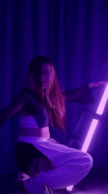 Dikey. Baştan çıkarıcı dans eden seksi kadın. Titreyen bir dansçı, canlı mor ve mavi ışıkla yıkanmış, canlı neon bir üçgenin altında sahnenin enerjisini somutlaştırıyor. Bir sanatçının kadın vücudu.