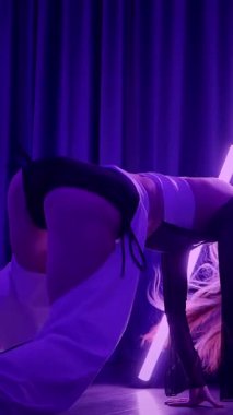 Dikey. Baştan çıkarıcı dans eden seksi kadın. Titreyen bir dansçı, canlı mor ve mavi ışıkla yıkanmış, canlı neon bir üçgenin altında sahnenin enerjisini somutlaştırıyor. Bir sanatçının kadın vücudu.