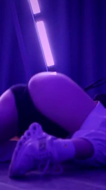 Dikey. Baştan çıkarıcı dans eden seksi kadın. Titreyen bir dansçı, canlı mor ve mavi ışıkla yıkanmış, canlı neon bir üçgenin altında sahnenin enerjisini somutlaştırıyor. Bir sanatçının kadın vücudu.