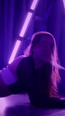 Dikey. Baştan çıkarıcı dans eden seksi kadın. Titreyen bir dansçı, canlı mor ve mavi ışıkla yıkanmış, canlı neon bir üçgenin altında sahnenin enerjisini somutlaştırıyor. Bir sanatçının kadın vücudu.