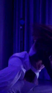 Dikey. Baştan çıkarıcı dans eden seksi kadın. Titreyen bir dansçı, canlı mor ve mavi ışıkla yıkanmış, canlı neon bir üçgenin altında sahnenin enerjisini somutlaştırıyor. Bir sanatçının kadın vücudu.