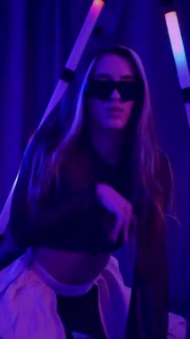 Dikey. Baştan çıkarıcı dans eden seksi kadın. Titreyen bir dansçı, canlı mor ve mavi ışıkla yıkanmış, canlı neon bir üçgenin altında sahnenin enerjisini somutlaştırıyor. Bir sanatçının kadın vücudu.