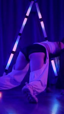 Dikey. Baştan çıkarıcı dans eden seksi kadın. Titreyen bir dansçı, canlı mor ve mavi ışıkla yıkanmış, canlı neon bir üçgenin altında sahnenin enerjisini somutlaştırıyor. Bir sanatçının kadın vücudu.