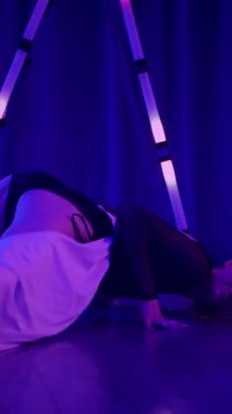 Dikey. Baştan çıkarıcı dans eden seksi kadın. Titreyen bir dansçı, canlı mor ve mavi ışıkla yıkanmış, canlı neon bir üçgenin altında sahnenin enerjisini somutlaştırıyor. Bir sanatçının kadın vücudu.