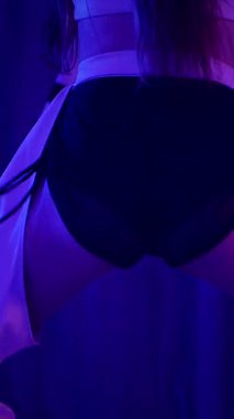 Dikey. Baştan çıkarıcı dans eden seksi kadın. Titreyen bir dansçı, canlı mor ve mavi ışıkla yıkanmış, canlı neon bir üçgenin altında sahnenin enerjisini somutlaştırıyor. Bir sanatçının kadın vücudu.