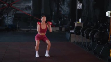 Dambılları başının üstüne sertçe kaldıran bir kadının karın kasları. Bir sporcunun kardiyo eğitimi ve sporu.