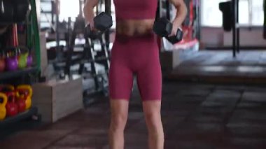 Dambılları başının üstüne sertçe kaldıran bir kadının karın kasları. Bir sporcunun kardiyo eğitimi ve sporu.