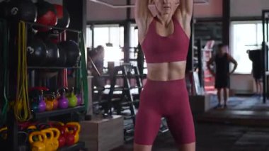 Dambılları başının üstüne sertçe kaldıran bir kadının karın kasları. Bir sporcunun kardiyo eğitimi ve sporu.