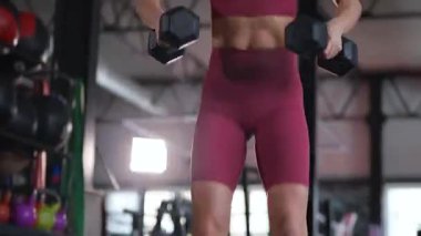 Dambılları başının üstüne sertçe kaldıran bir kadının karın kasları. Bir sporcunun kardiyo eğitimi ve sporu.