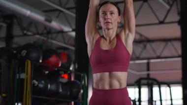 Dambılları başının üstüne sertçe kaldıran bir kadının karın kasları. Bir sporcunun kardiyo eğitimi ve sporu.