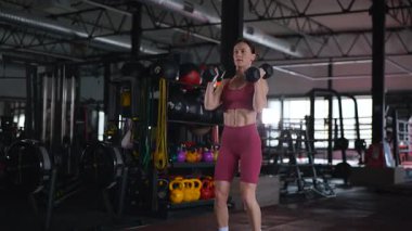 Dambılları başının üstüne sertçe kaldıran bir kadının karın kasları. Bir sporcunun kardiyo eğitimi ve sporu.
