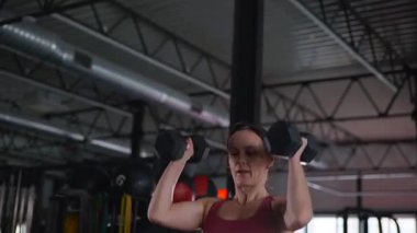 Dambılları başının üstüne sertçe kaldıran bir kadının karın kasları. Bir sporcunun kardiyo eğitimi ve sporu.