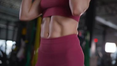 Dambılları başının üstüne sertçe kaldıran bir kadının karın kasları. Bir sporcunun kardiyo eğitimi ve sporu.