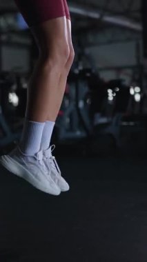 Dikey. Güçlü bir form, odaklanmış ip atlama seansı. Atletizm iş başında, yerçekimine meydan okuyan bir kadın. Spor salonunun karanlık kalbi, hareketli bir egzersiz patlaması..