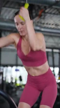 Dikey. Spor salonundaki fitness kadını simülatörde ipleri geriyor. Güzel bir atletik figürlü ve şortlu bir kadın antrenman yapıyor..