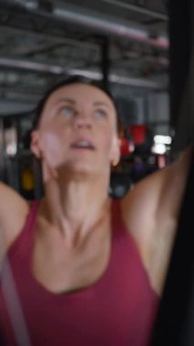Dikey. Spor salonundaki fitness kadını simülatörde ipleri geriyor. Güzel bir atletik figürlü ve şortlu bir kadın antrenman yapıyor..