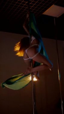 Dikey. Bir kadın ve Teal ipeği bir direğin etrafında dans ediyorlar, büyüleyici bir görüntü. Direk dansı. Karanlıkta asılı kalan bir dansçının zarafeti ortaya çıkar. Bir sanatçının sanatı, stüdyo ışığıyla aydınlatılır..