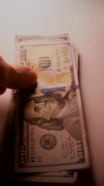 Dikey. Yüz dolarlık banknotların yakın plan görüntüsü. Karmaşık ayrıntıları ince aydınlatılmış. Eller dikkatlice sayıyor, 100 dolarlık banknotlar, yumuşak, sıcak bir ışıkta yıkanmış..