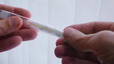 Nazikçe tutulan cıvalı bir termometre sıcaklığı gösterir. Cam tüp, tanıdık bir alet, vücut ısısını gösterir. Sağlıklı bir insanın sıcaklığı 36.6 'dır..