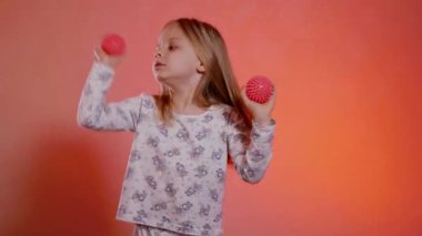 Desenli pijamalı genç kız iki pembe top tutuyor ve onlarla gözlerini kapıyor, mutlu bir şekilde dans ediyor ve oynuyor..